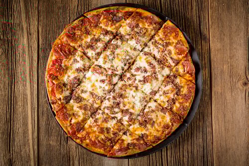 Pizza on wood counter with meat toppings under cheese.