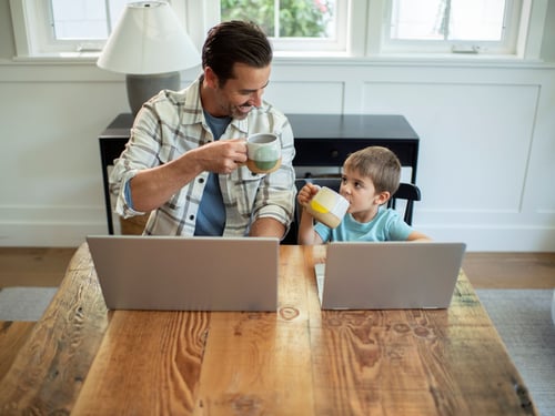 Father and son at kitchen table with laptop drinking coffee