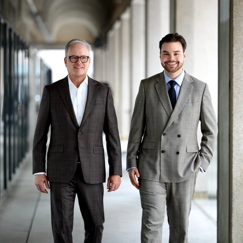 A father and son walking in suits down an outdoor covered passage.