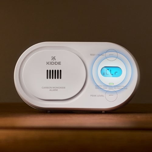 A CO alarm with a screen lit, showing clear. Circles highlight the display.