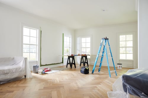 Image of a room undergoing renovation, with a ladder in the middle of the room, under a smoke alarm that was just installed.