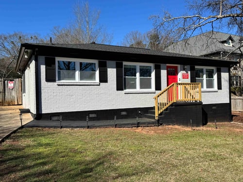Brick building painted white and black with a red door and wooden steps. surrounded by grass and blue sky