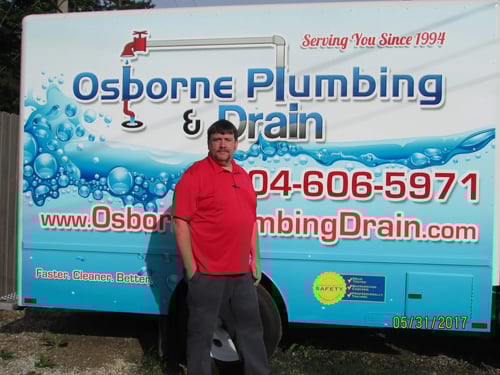 Technician in red shirt posed by Osborne Plumbing & Drain service van wrap with logo and phone number.