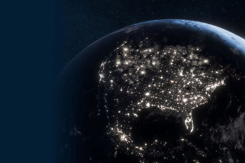 Earth at night from space, showing city lights across continents and oceans.