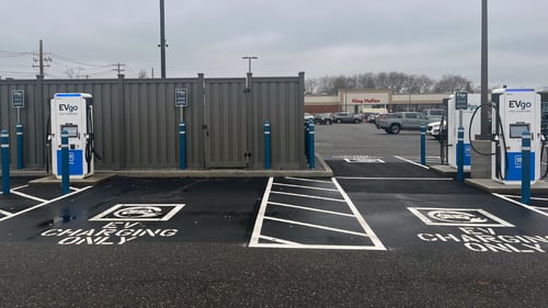 Several EVgo fast-charging units installed in marked parking spaces at a public charging station, with EVgo logos on the chargers, protective bollards around each unit