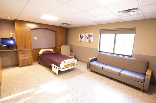 The labor and delivery room with a bed, pull-out sofa, storage cabinets, TV and bassinet.