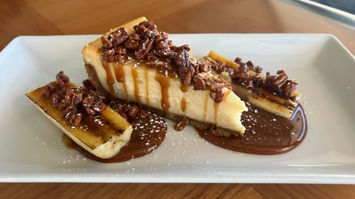 Photo showing three slices of cheesecake with candied pecans, banana rum caramel and whipped cream.