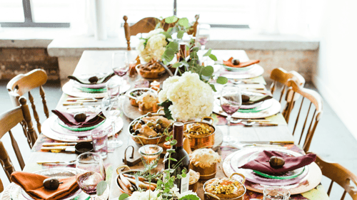 A beautifully set dining table adorned with vibrant plates, elegant glassware, and an array of dishes, complemented by flowers and greenery.