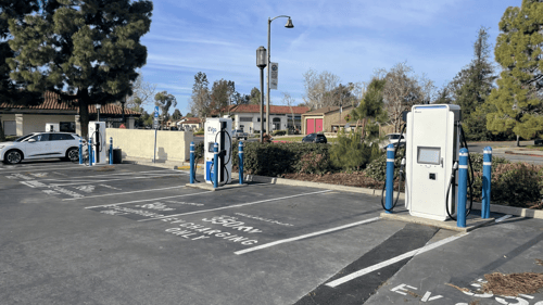 Several EVgo fast-charging units installed in marked parking spaces at a public charging station, with EVgo logos on the chargers, protective bollards around each unit