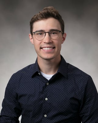 Zachary Kraft smiling in front of a gray background.
