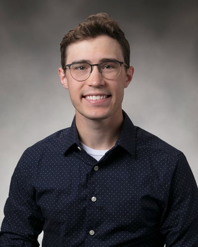 Zachary Kraft smiling in front of a gray background.