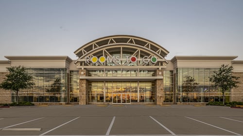 Rooms To Go furniture store facade at sunset in Round Rock, TX, featuring expansive glass windows and modern architectural design.