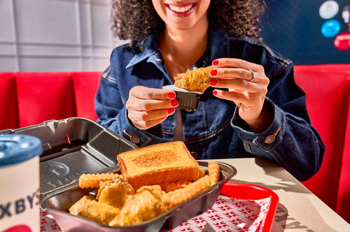 Woman dipping fried chicken wing in ranch sauce with a wing meal in front of her on the table including crinkle fries, texas toast, and a drink.
