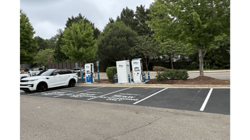 Several EVgo fast charging units installed in marked parking spaces at a public charging station, with EVgo logos on the chargers, protective bollards around each unit.