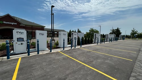 12 EVgo fast charging units installed in marked parking spaces at a public charging station, with EVgo logos on the chargers, protective bollards around each unit