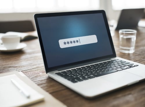 Silver laptop on a desk top with a password field on-screen.