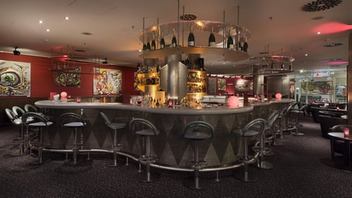 Checkpoint Bar im Maritim proArte Hotel Berlin – Große, gemütliche Bar mit stilvollen schwarzen Ledersesseln, Samtsesseln und eleganten Hockern. Die moderne Kunst an den Wänden schafft ein einzigartiges, einladendes Ambiente direkt an der Friedrichstraße.
