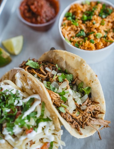 Two tacos filled with seasoned meat, served with Mexican rice and salsa on the side.