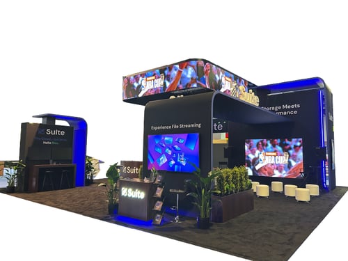 Trade show booth with Suite branding, digital display screens, seating area, plants, and illuminated signage.