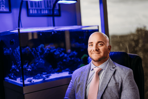 Agent John sitting wearing blue suit with fish tank in the back