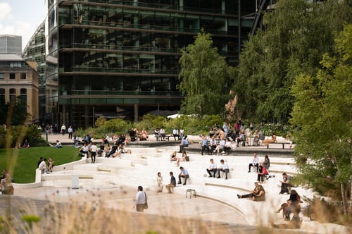 People sitting in Exchange Square surrounded by tall buildings and greenery