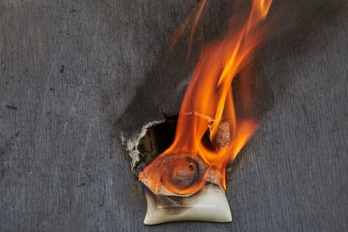 Close-up of a fire starting from an electrical outlet on a dark wall.