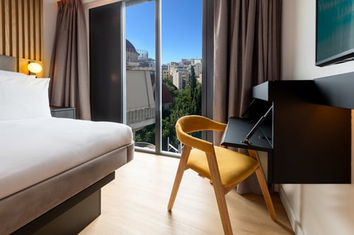 Inside a Grea Iras Apartment room with a view of the Acropolis through the window.
