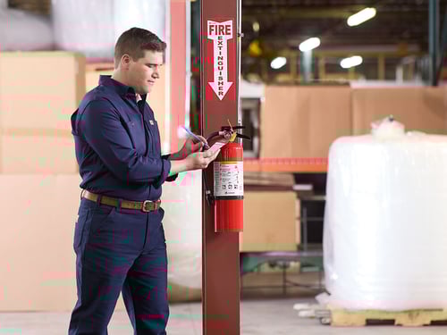 A man inspects a fire extinguisher mounted to a pole.