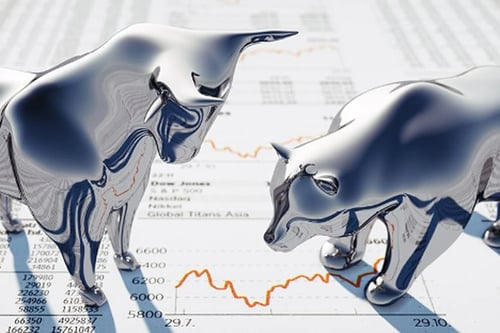 Chrome bear and bull statues standing on top of a printout of numbers and graphs.