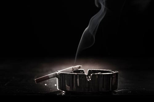 A close-up shot of a cigarette resting on an ashtray, with a delicate wisp of smoke rising, highlighting the fire risk associated with smoking.