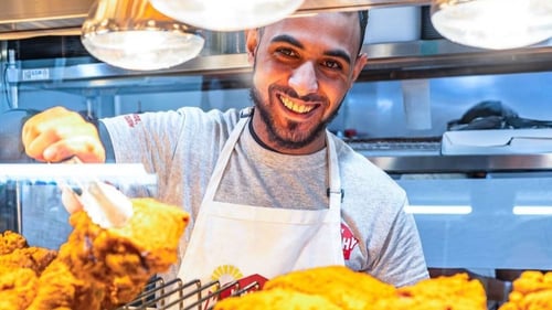 A smiling man holds a tray filled with golden fried chicken, showcasing a joyful moment of culinary delight.