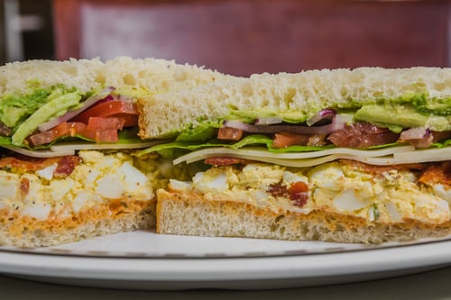 Hell's Kitchen Sandwich served on Sourdough bread with egg salad, bacon, swiss cheese, avocado, Heidi's Cajun Sauce, lettuce, tomato, and onion