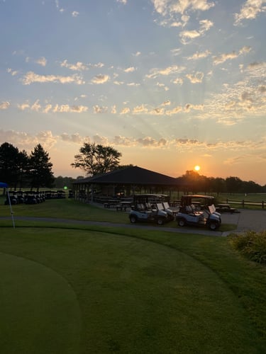 Golf carts lined up in the morning at Audubon Golf Course with practice putting green and fairways in background.