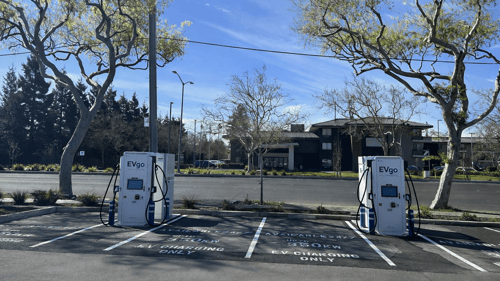 Several EVgo fast-charging units installed in marked parking spaces at a public charging station, with EVgo logos on the chargers, protective bollards around each unit