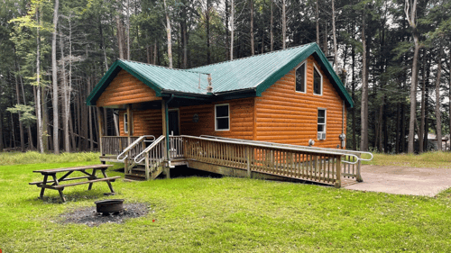 brown cabin with green roof next to a picnic bench and fire pit