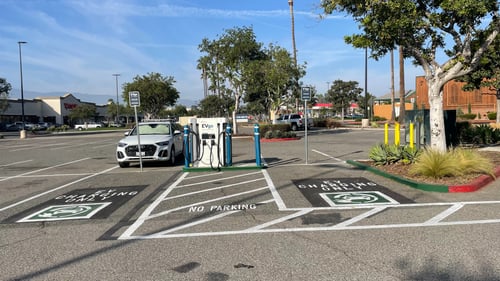 EVgo fast-charging unit installed in marked parking spaces at a public charging station, with EVgo logo on the charger, protective bollards around the unit.