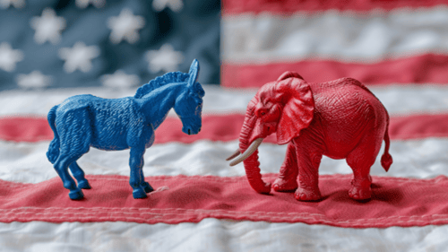 A blue donkey and a red elephant figurine facing each other against a backdrop of an American flag.