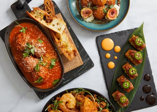 Seafood and italian dishes on a white marble table including oysters, brushetta, meatballs, and sushi.