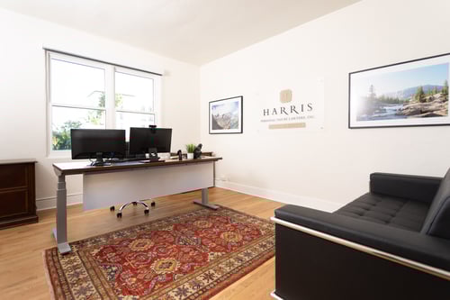 Harris Personal Injury Lawyers Santa Barbara Office Interior. There is an antique style rug on the ground. Two monitors sit on a desk. A modern black leather couch sits facing the desk. There are framed photos of mountain landscape views on either side of a "Harris Personal Injury Lawyers, Central Coast" sign.