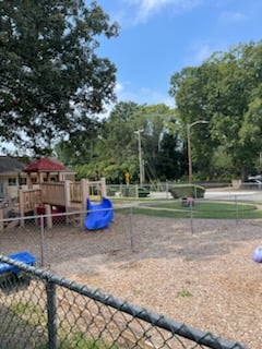 Wide shot of an empty playground with slides, climbing structures, and swings in a sunny outdoor space.