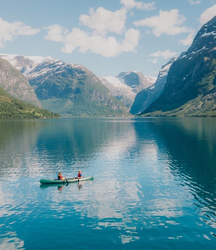 Image of two people canoeing on lake in front of mountains