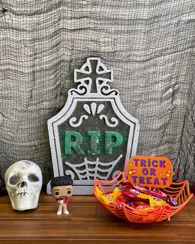 A Halloween display featuring a gravestone marked "RIP," a colorful "Trick or Treat" sign, and a basket of candy.