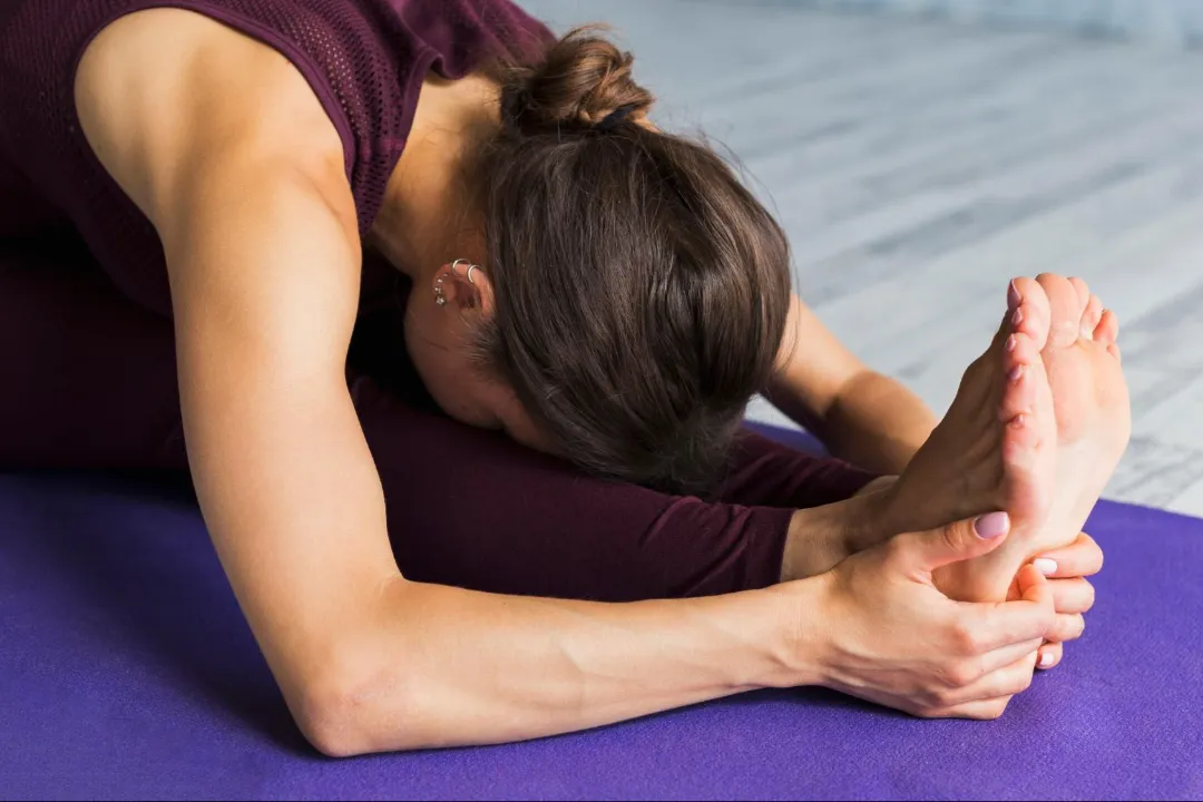 woman stretching on yoga mat holding her foot