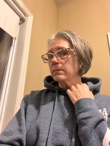 Selfie of Colleen, wearing a hoodie in front of a wall.