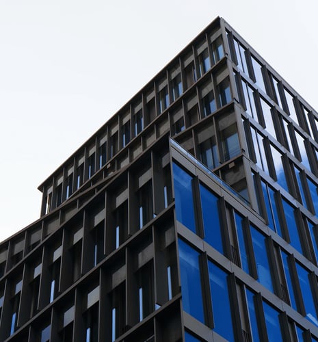 Modern building corner with reflective blue glass windows against a clear sky. The structure features sleek, geometric lines and a minimalist design.