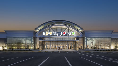 Exterior view of the Rooms To Go store in Daytona Beach, Florida, at dusk, featuring large glass windows and illuminated signage.