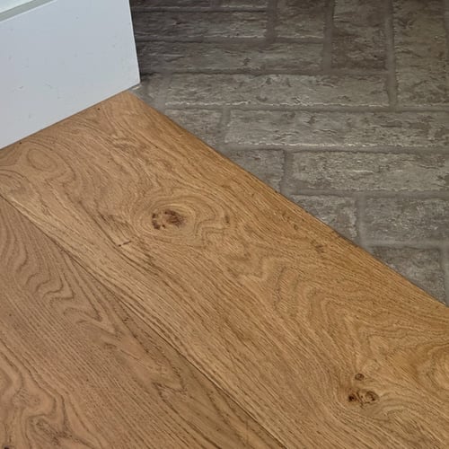 Close-up of wide-plank character-grade white oak hardwood flooring meeting a grey brick entryway in a Sugar City, Idaho home.
