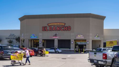 People with yellow shopping carts in a full parking lot of El Rancho Supermarcado