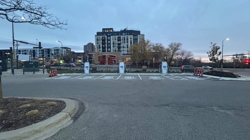 Several EVgo fast-charging units installed in marked parking spaces at a public charging station, with EVgo logos on the chargers, protective bollards around each unit