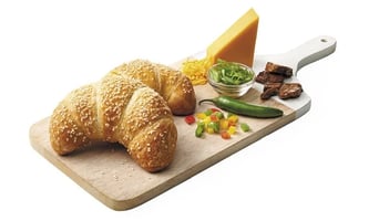 A croissant filled with grilled beef, serrano chili sauce, tri-colored bell peppers, green onions, cheddar cheese and sprinkled with sesame seeds
